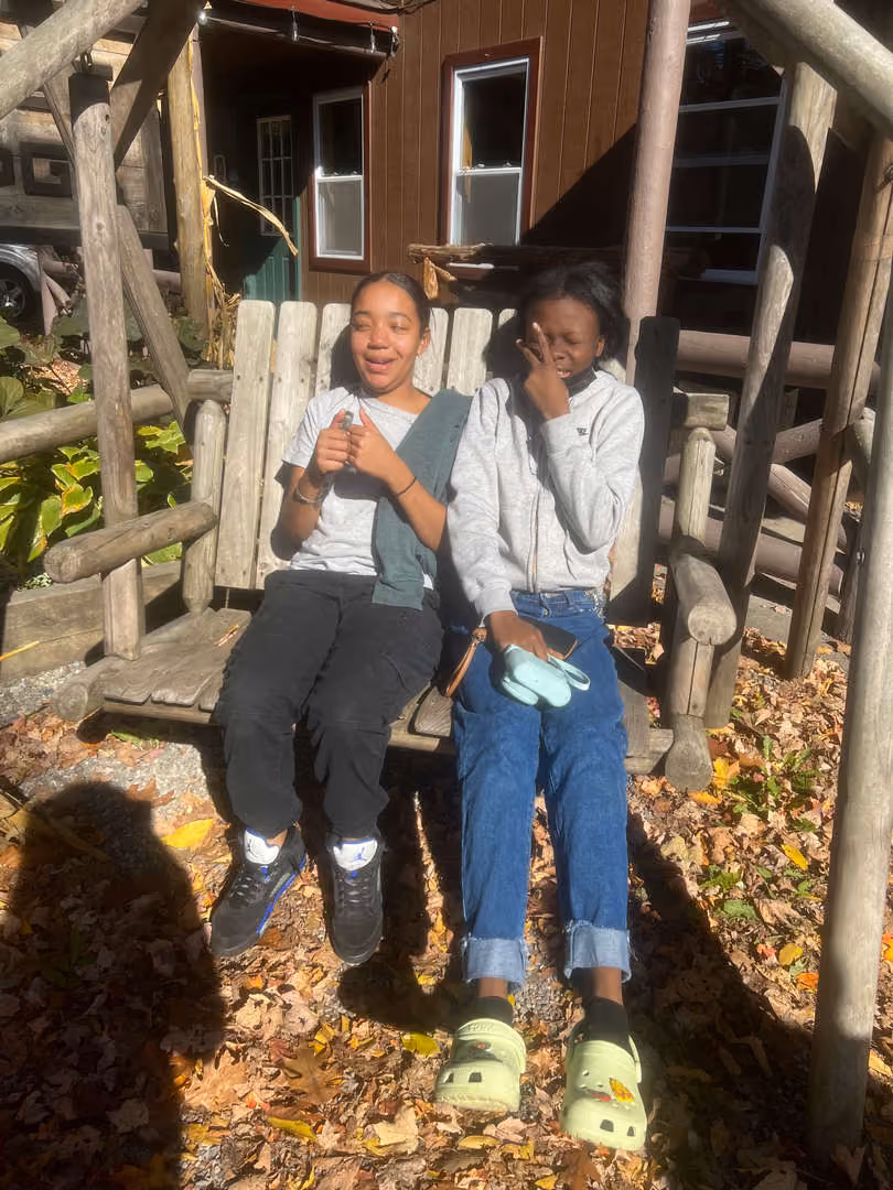 Two students sitting together on a wooden bench outdoors during fall