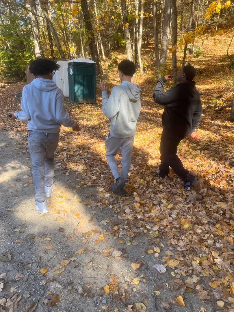 Three students playing outdoors among autumn leaves in a wooded area