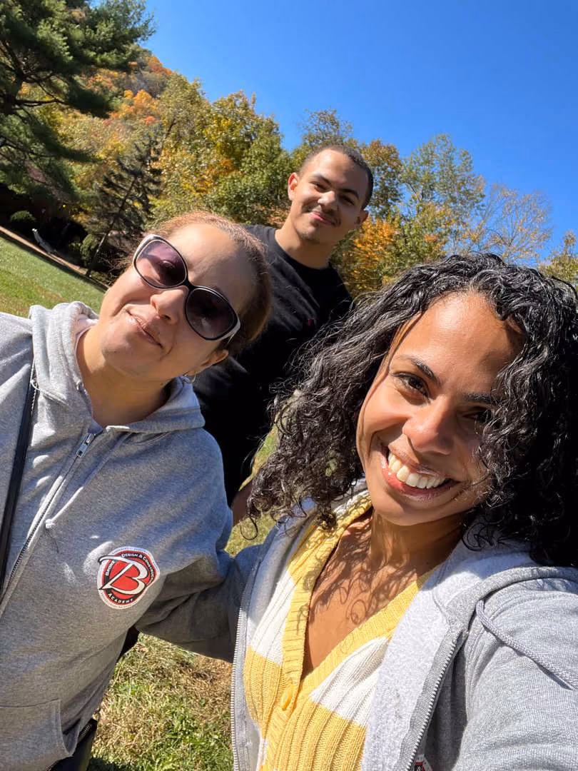 Three students smiling outdoors during fall foliage field trip