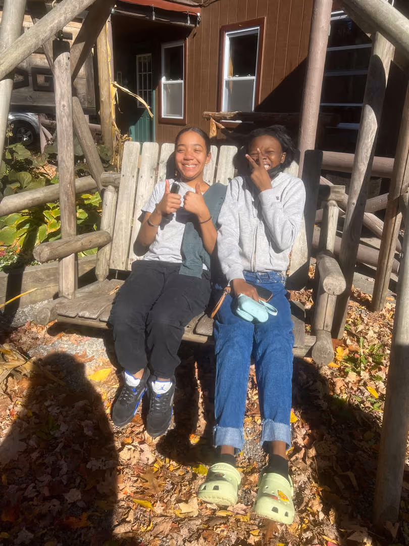 Two students smiling on a wooden bench during fall outdoor trip