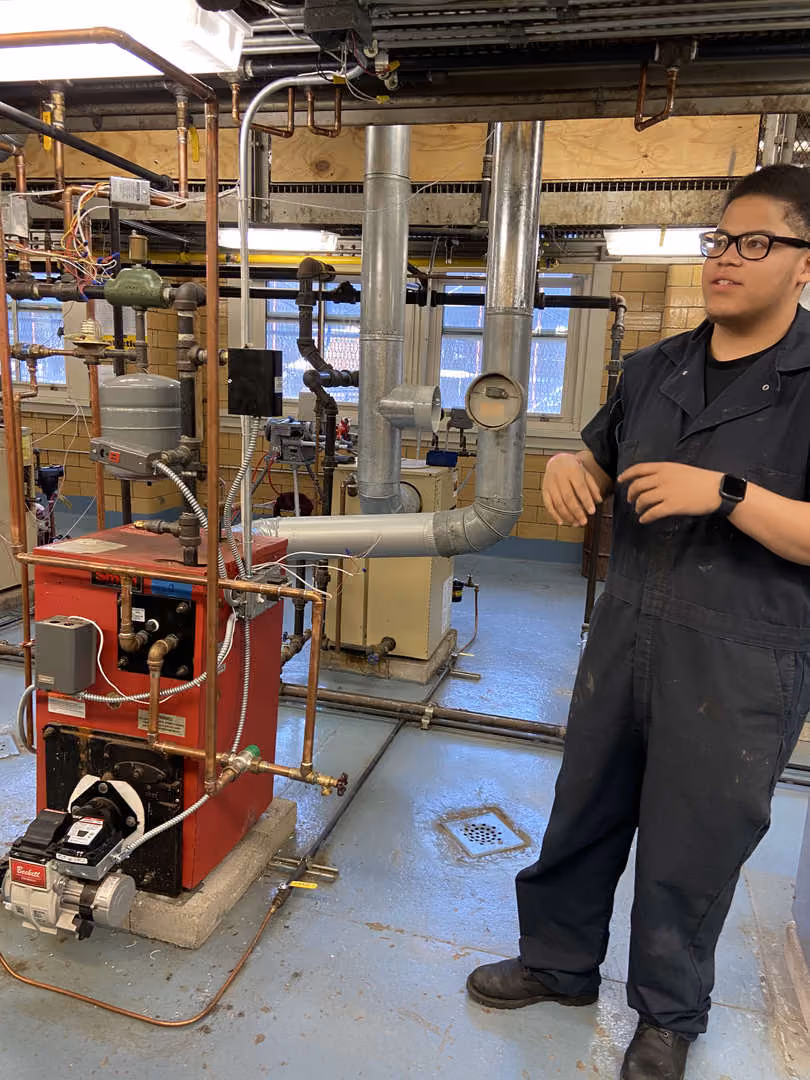 Student in coveralls standing beside boiler equipment in HVAC lab
