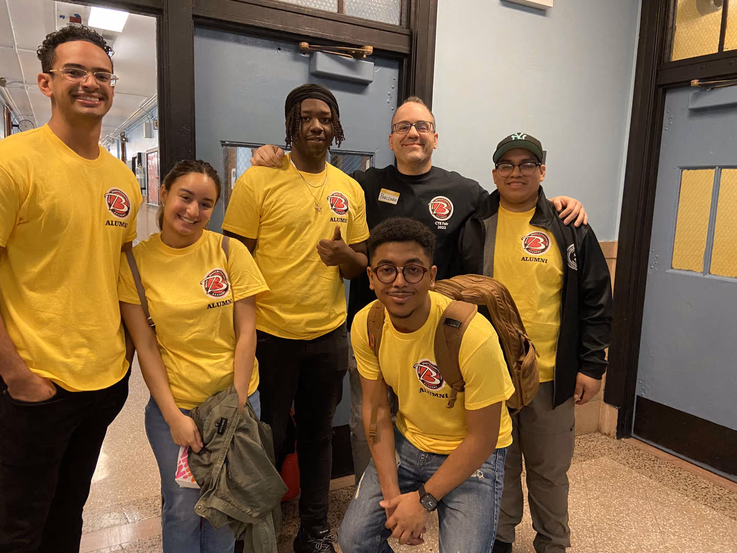 Alumni students and staff posing together in school hallway