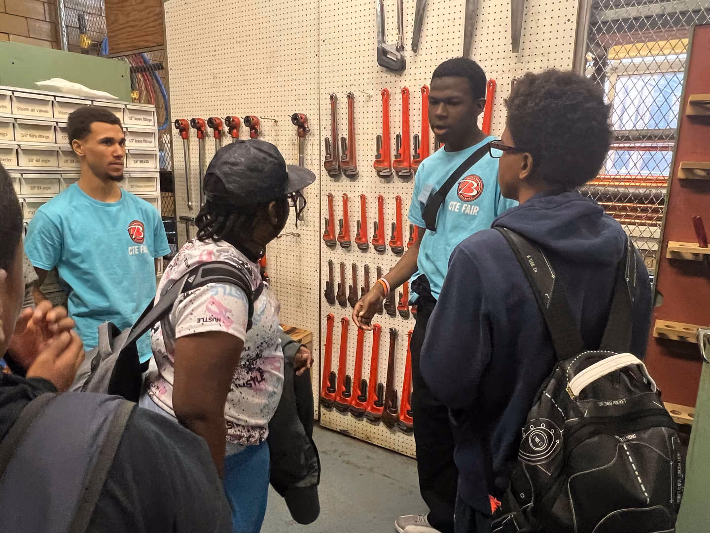 CTE Fair students explain plumbing tools to visiting peers in workshop
