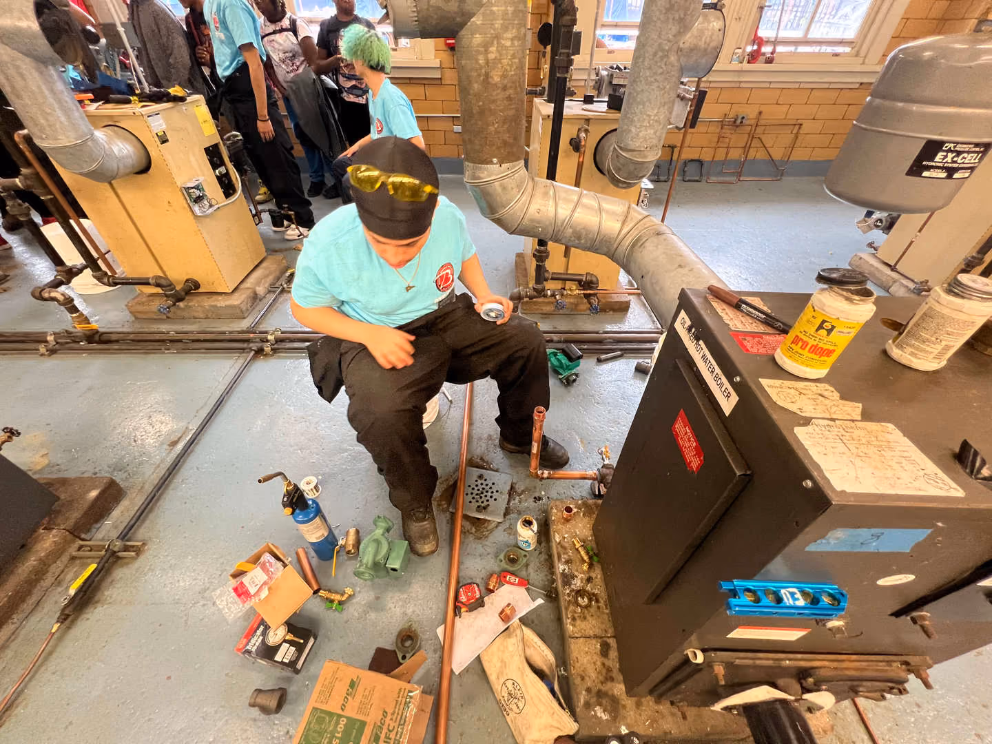 Student in safety glasses working on plumbing pipes in vocational classroom