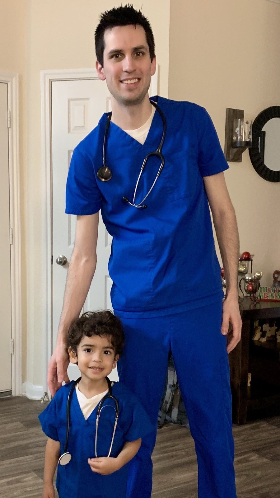 Samuel Baker, RN, in scrubs with his young son, who is wearing matching scrubs and a toy stethoscope