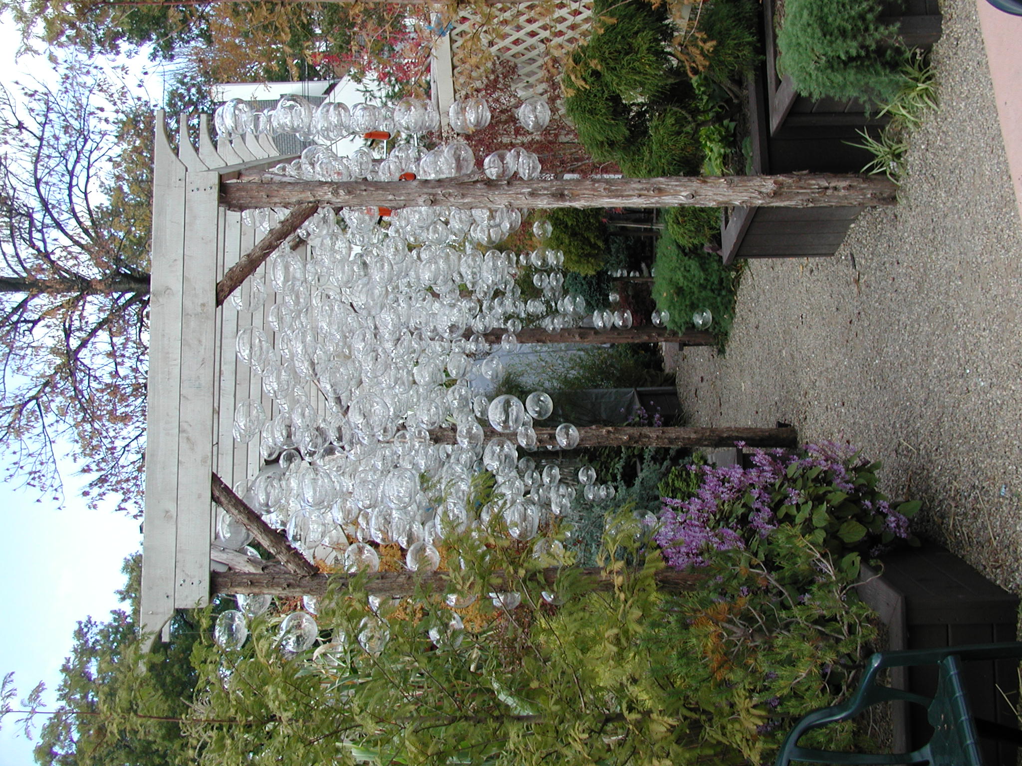 Gravel pathway beneath a pergola hung with clear glass spheres.