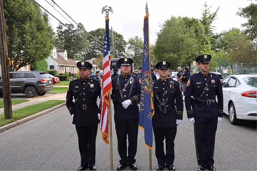 Four police officers in uniform on a street, two holding American and state flags.