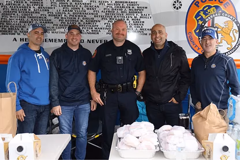 Five men, including a police officer, standing behind tables with food packages and drinks indoors.