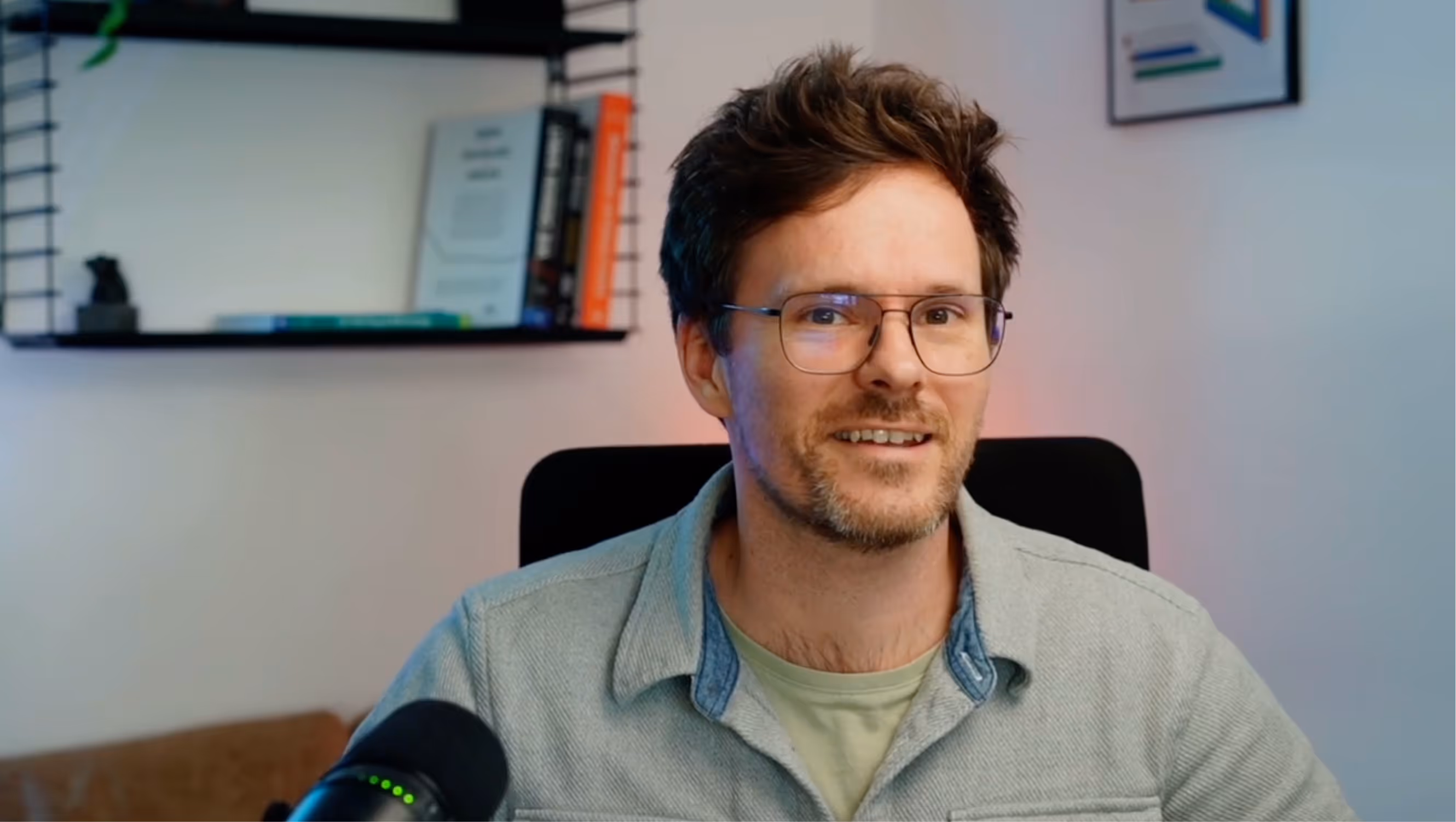 Man with glasses speaking into a microphone during a video interview