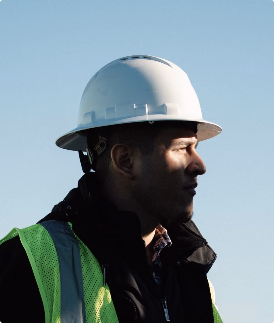 Construction worker in a white hard hat and safety vest in profile