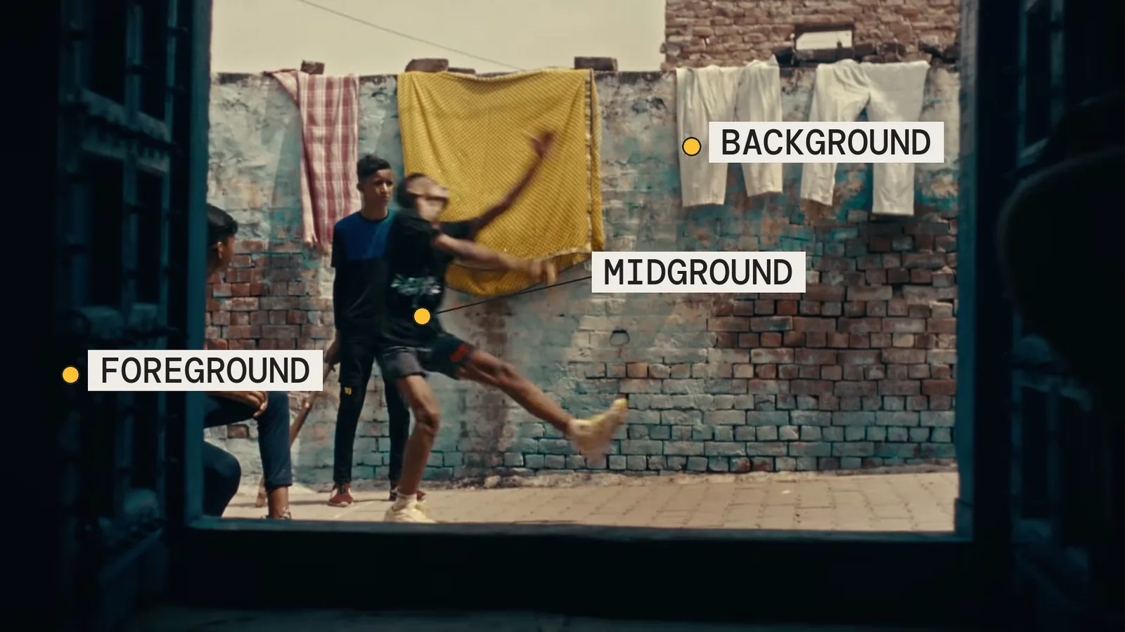 Frame at 00:27 of the Air India AI film, labelled in three planes: a dark window frame in the foreground, boys playing cricket in the midground, washing hung on a brick wall in the background