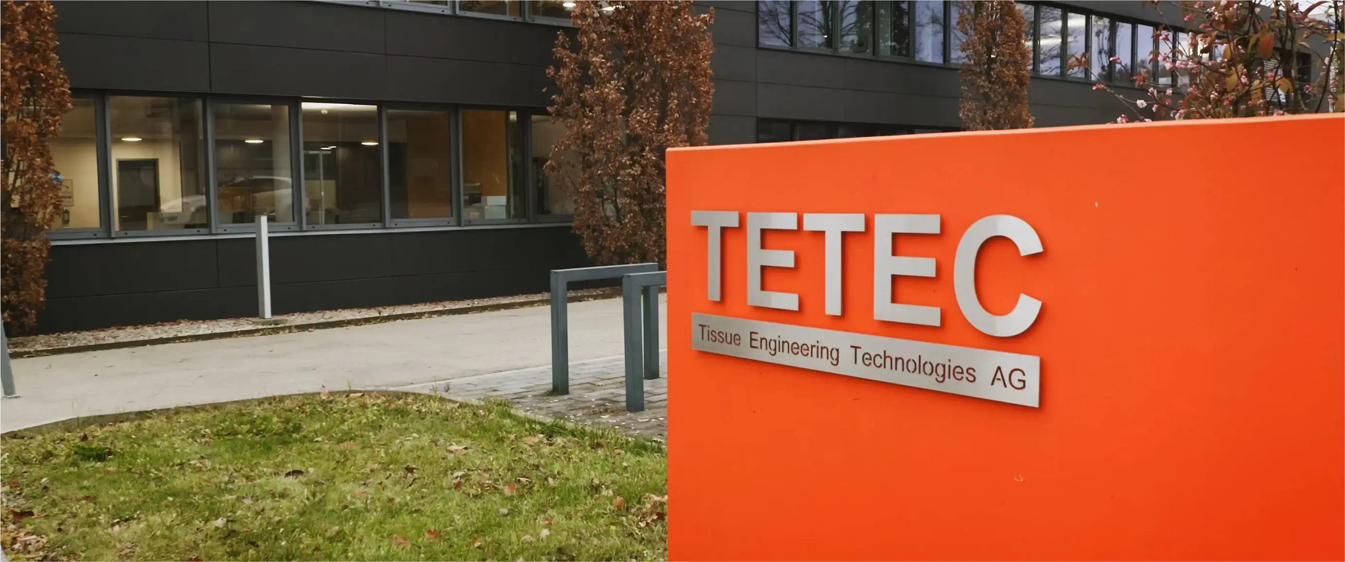 Oranges Firmenschild von TETEC Tissue Engineering Technologies AG vor modernem Bürogebäude.
