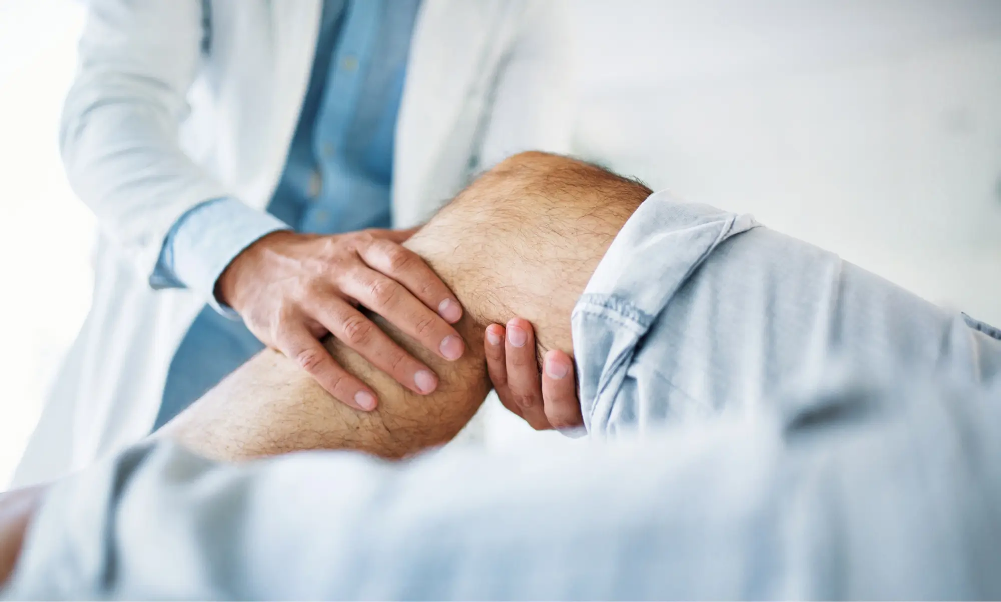 Arzt untersuchtes das gebeugte Knie eines Patienten mit beiden Händen.