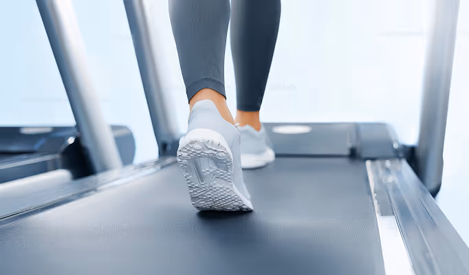 Person in sports shoes walking on a treadmill with black leggings.