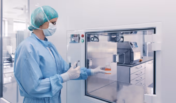 Laborantin in Schutzkleidung bedient sterile Laborapparatur mit einer Petrischale.