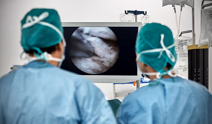 Zwei Chirurgen in Operationskleidung, die ein medizinisches Bild auf einem Monitor betrachten.