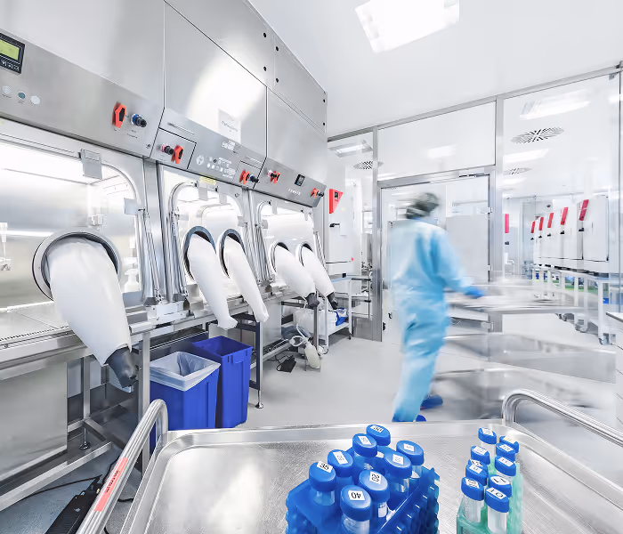 Reinraumlabor mit Isolatoren und Person in Schutzanzug bei Arbeit an sterilem Arbeitsplatz.