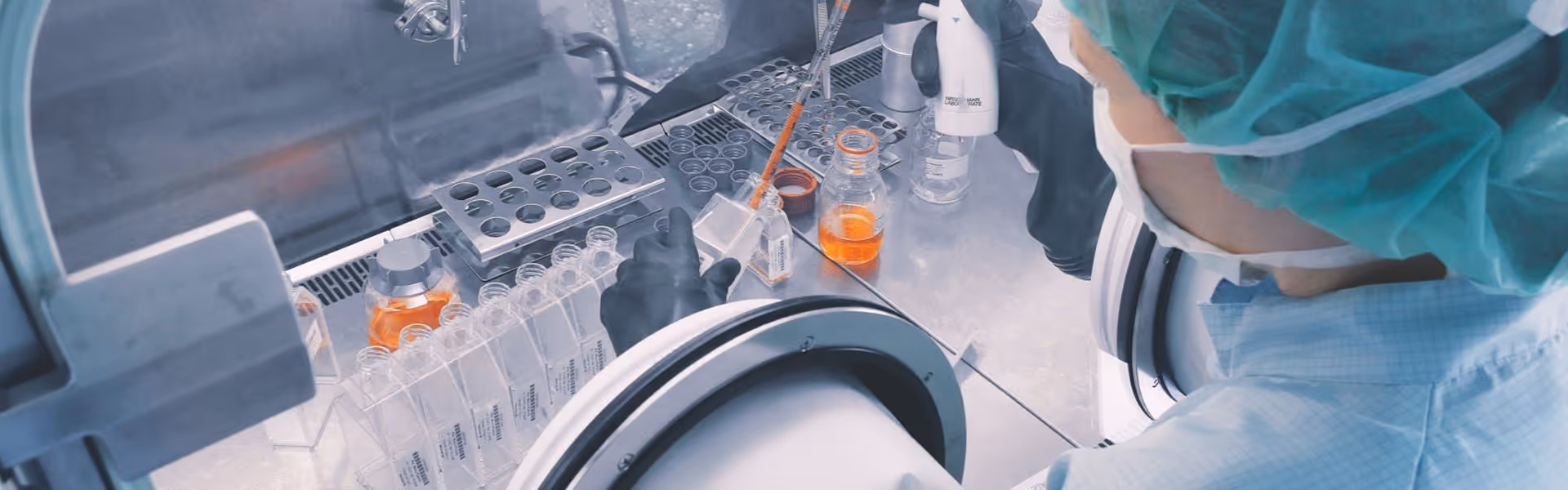 Wissenschaftler in Schutzkleidung arbeitet mit Pipette und Behältern in einer sterilen Laborumgebung.