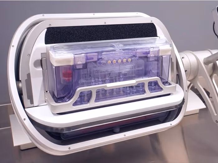 Transparent purple rectangular container inside a white, circular medical or lab device on a metallic table.
