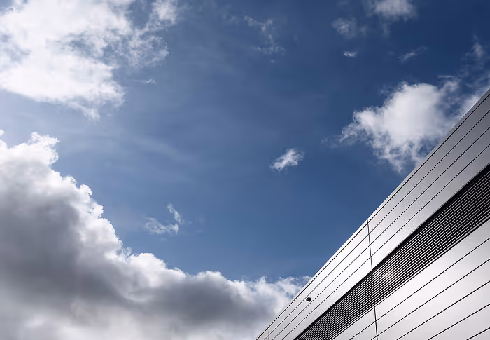 Blauer Himmel mit Wolken neben der metallischen Außenwand eines Gebäudes.