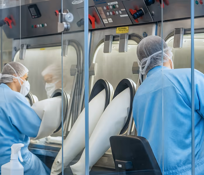 Zwei Laborarbeiter mit Schutzkleidung arbeiten an sterilem Handschuh-Isolator im Reinraum.
