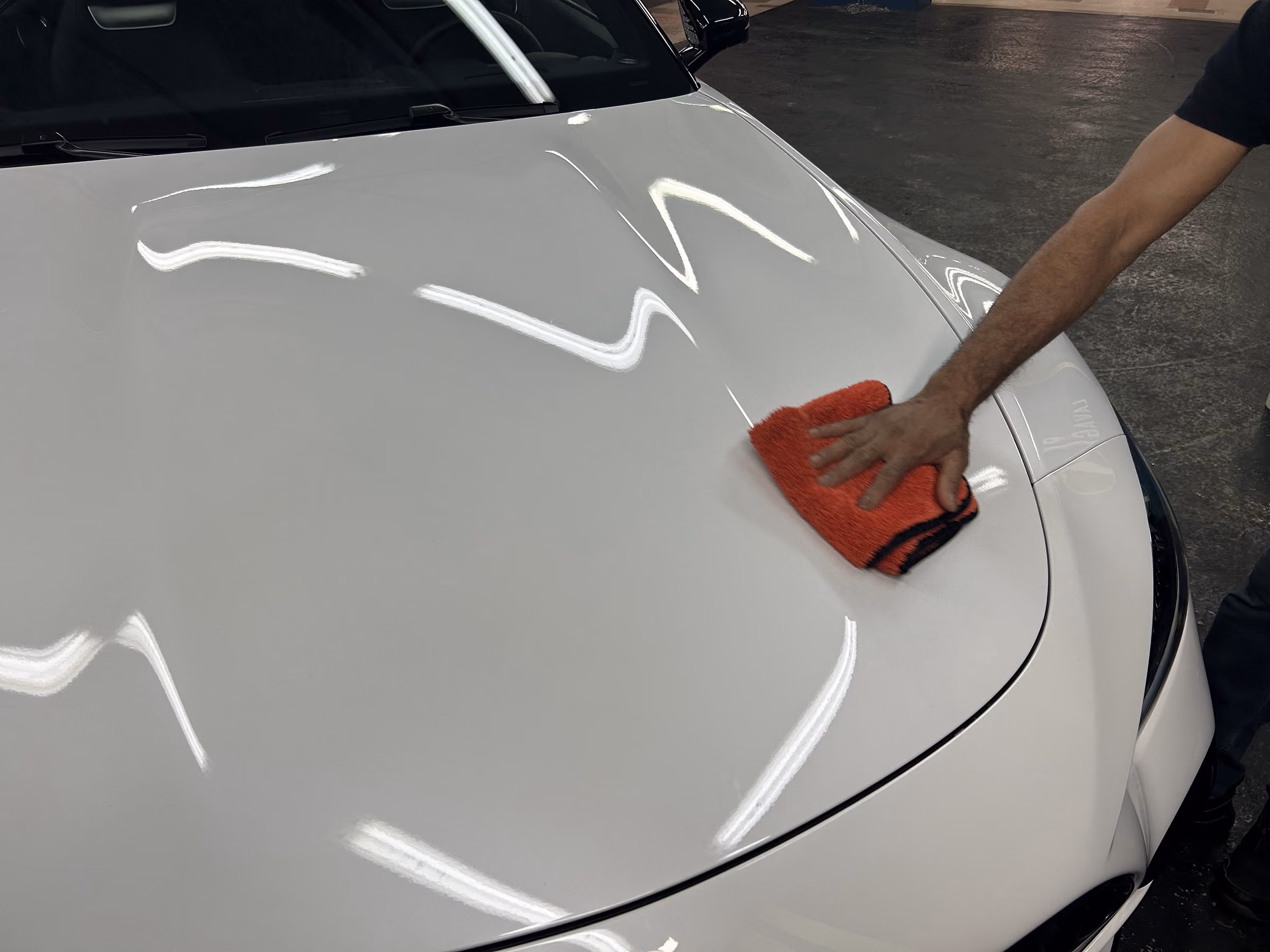 Passage de la microfibre à la main sur le capot d'un véhicule blanc dans l'atelier Bingo'z à Paris 15