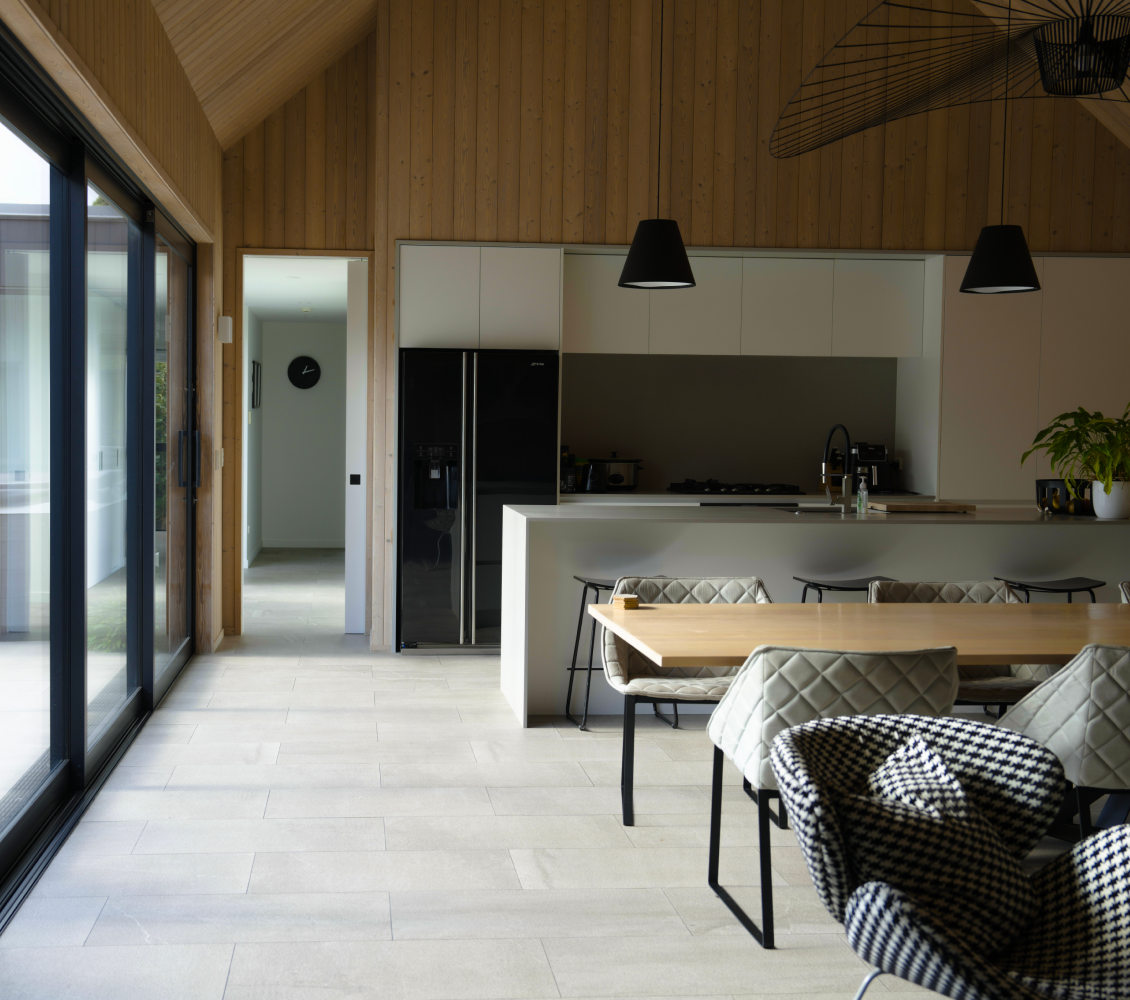 Modern kitchen with black refrigerator, island, wood dining table, patterned and cushioned chairs.