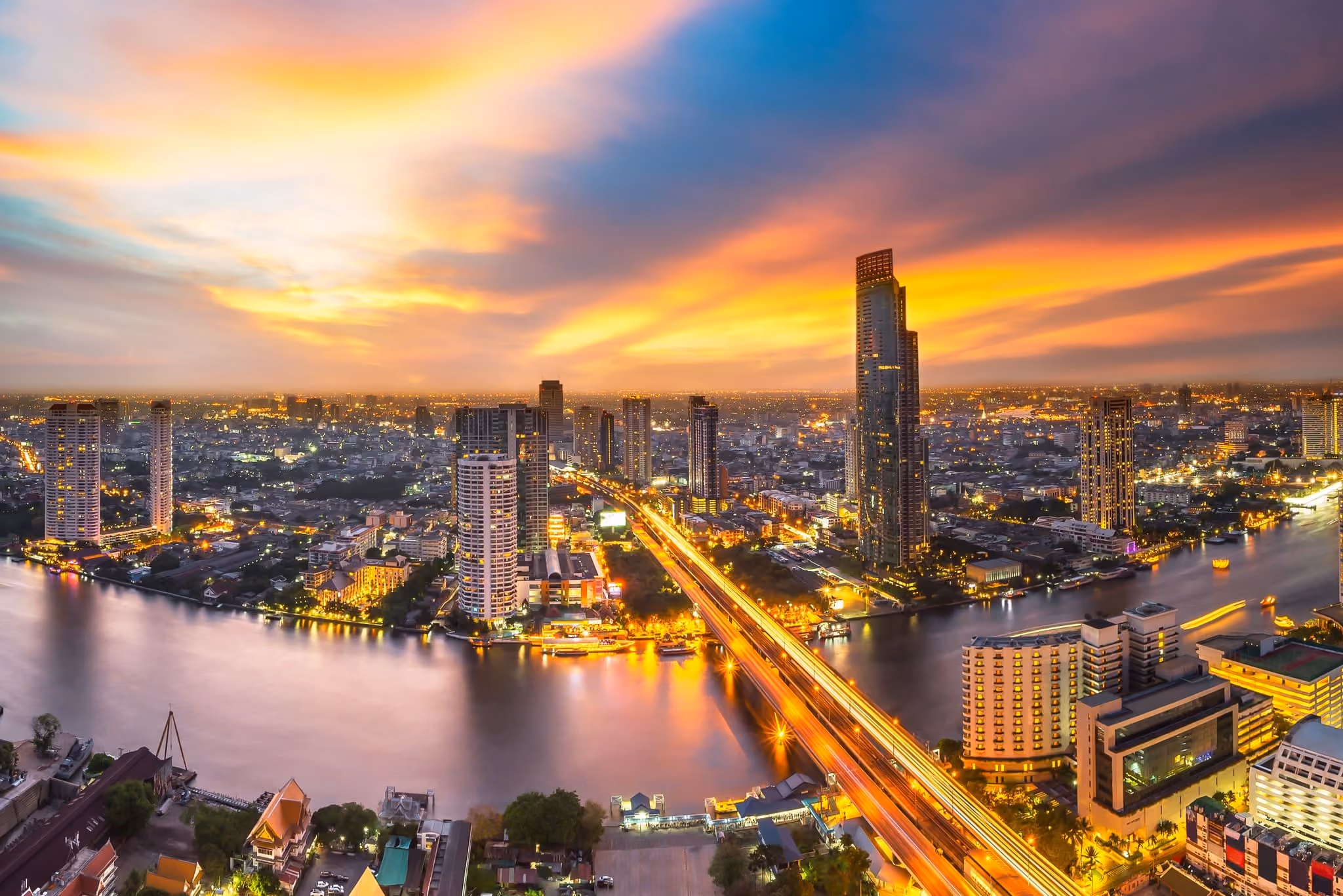 Bangkok's riverside skyline at sunset, with the Chao Phraya curving past lit high-rise towers