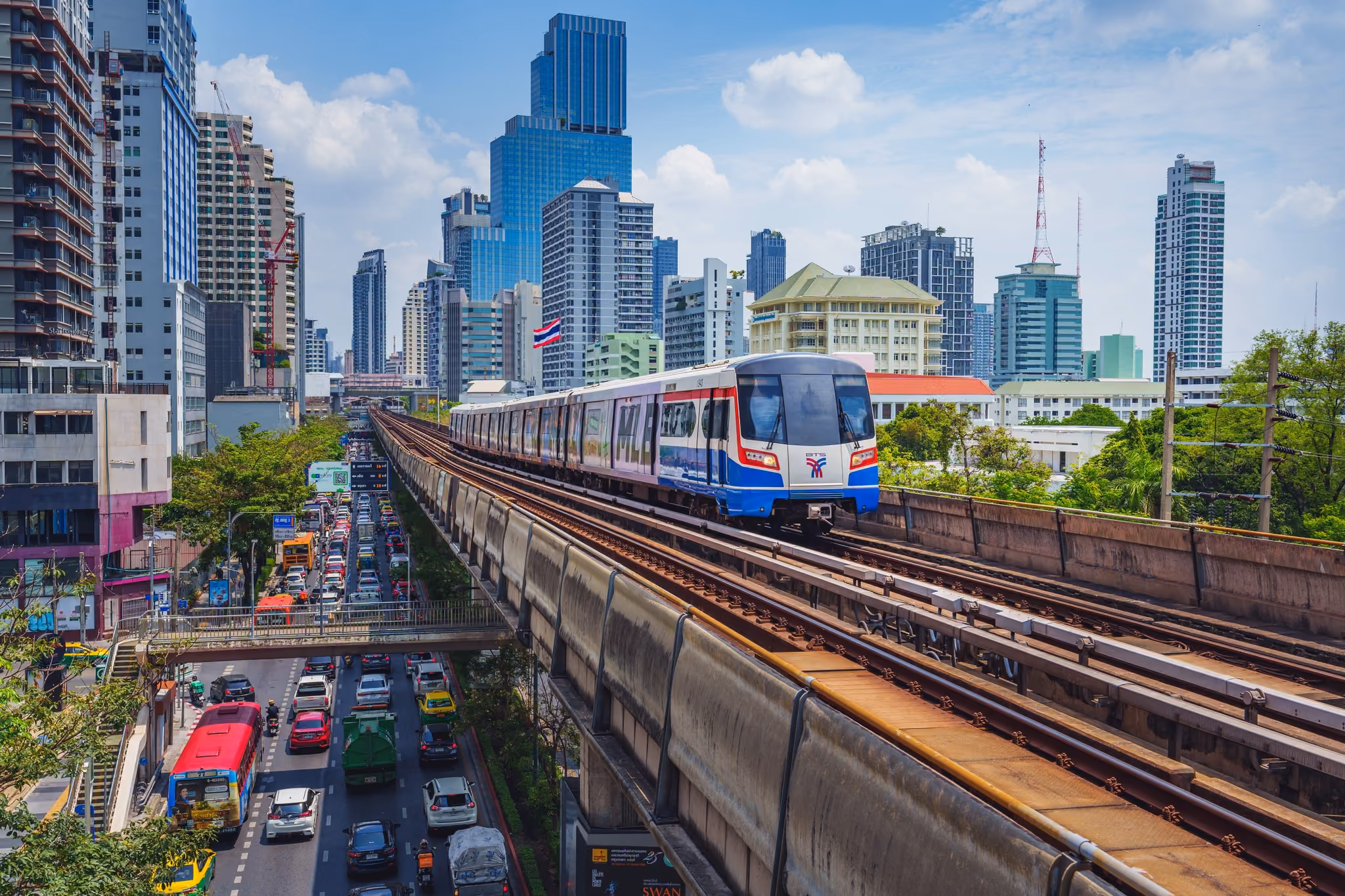 A BTS Skytrain on an elevated track above Bangkok traffic, with the skyline behind