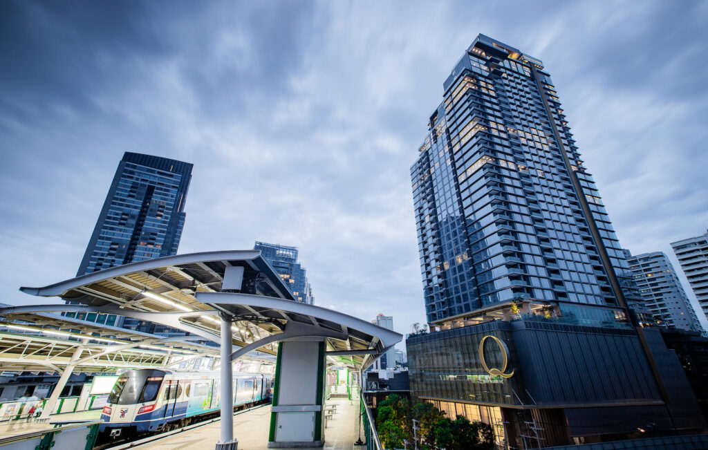 A BTS station platform canopy at Nana with the Q1 Sukhumvit tower rising behind it