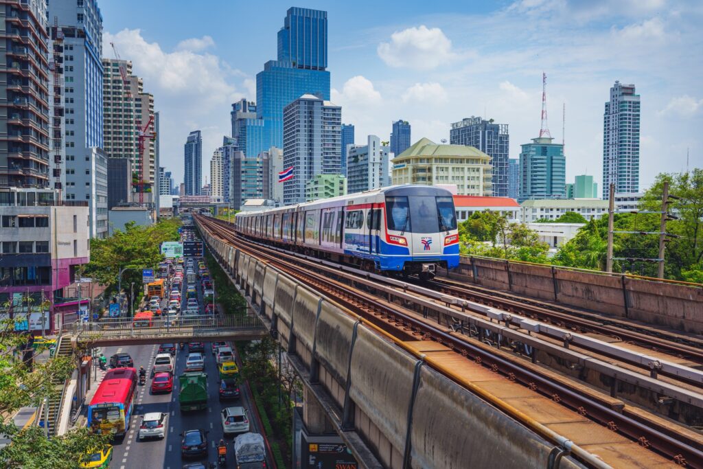 A BTS Skytrain on an elevated track above Bangkok traffic, with the skyline behind