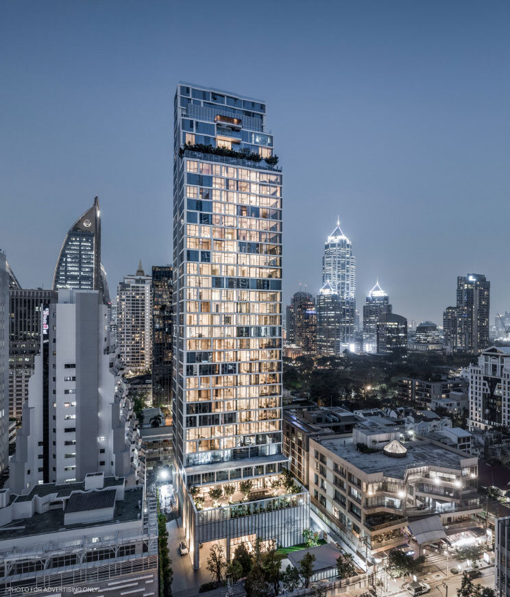 The slim SCOPE Langsuan tower lit at dusk above the surrounding Bangkok rooftops