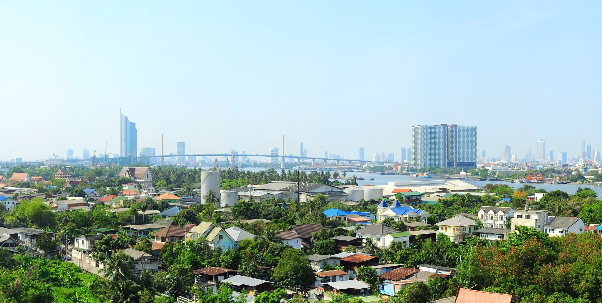 Low-rise suburban housing on the edge of Bangkok, with green gardens and the skyline in the distance