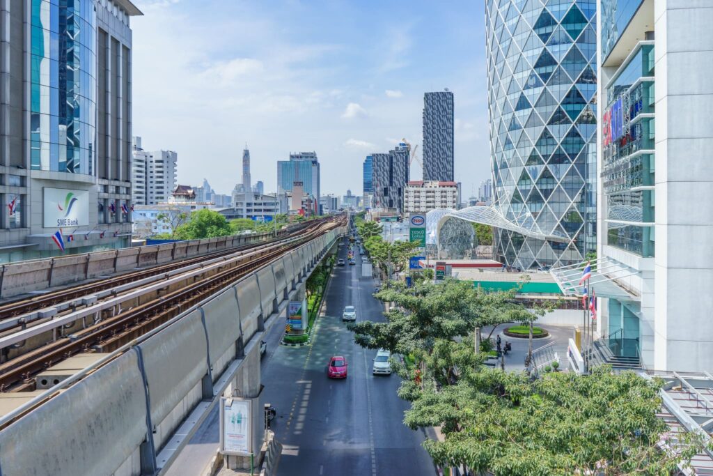 A tree-lined street in Ari with the BTS line running above modern low-rise buildings