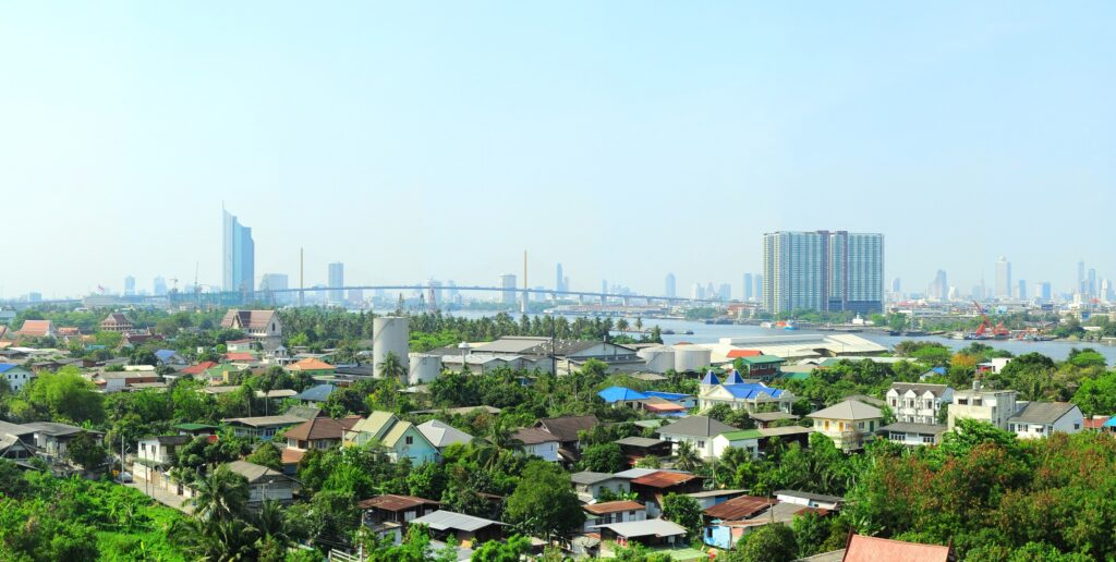 Low-rise suburban housing on the edge of Bangkok, with green gardens and the skyline in the distance