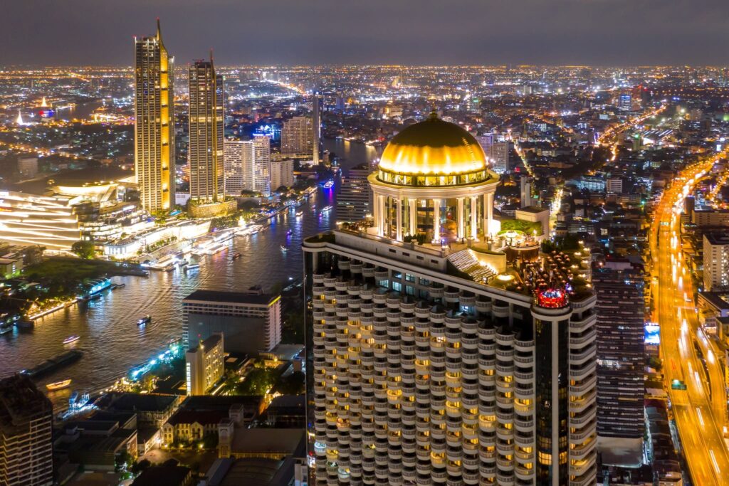 The Bangkok riverside at night, with the lit gold dome of State Tower above the Chao Phraya
