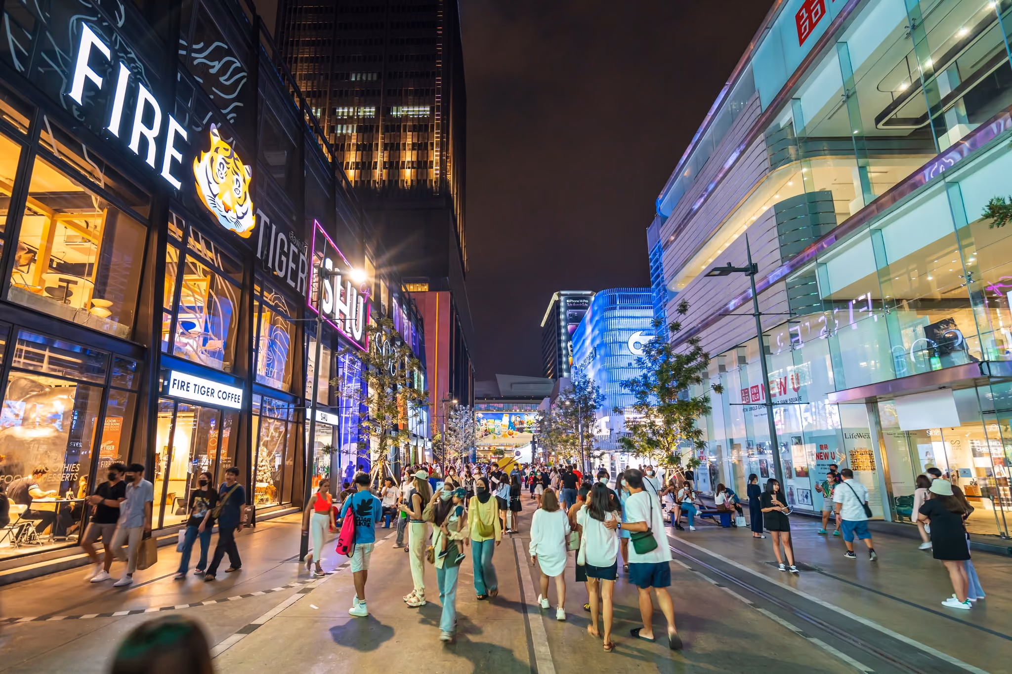 Shoppers walking through Siam Square at night, past lit storefronts and signage