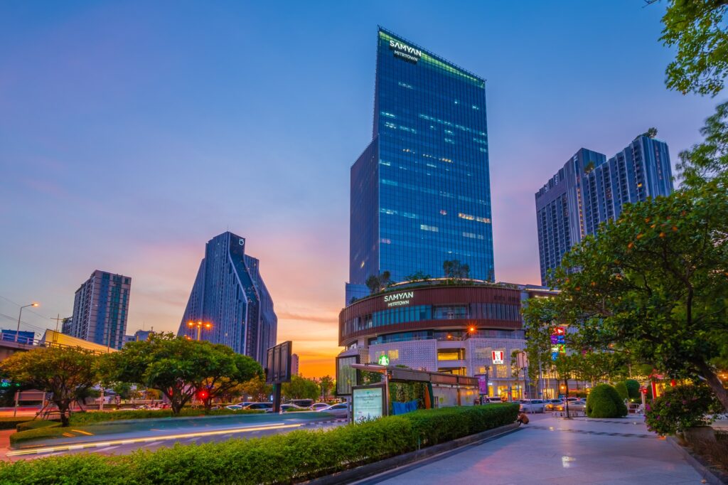 The green glass tower of Samyan Mitrtown at dusk, above its landscaped forecourt