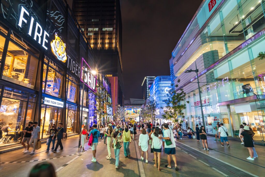 Shoppers walking through Siam Square at night, past lit storefronts and signage