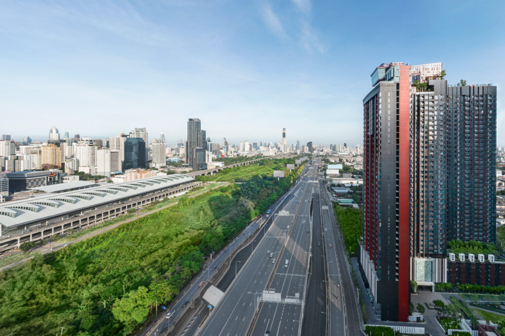 The Life Asoke Hype tower beside a wide road, with green space along its edge