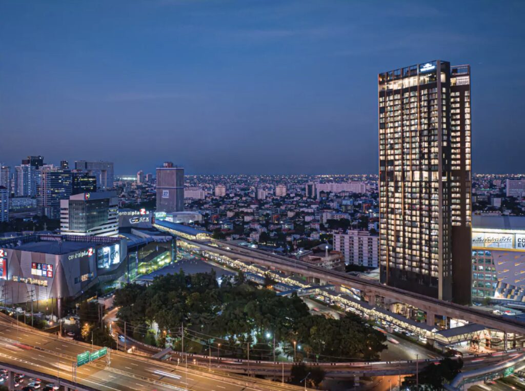 The Crest Park Residences tower at dusk above Lat Phrao, with parkland in the foreground