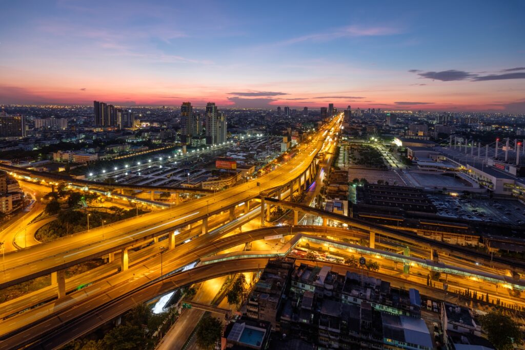 The Bang Na expressway interchange lit at dusk, its ramps curving over the district