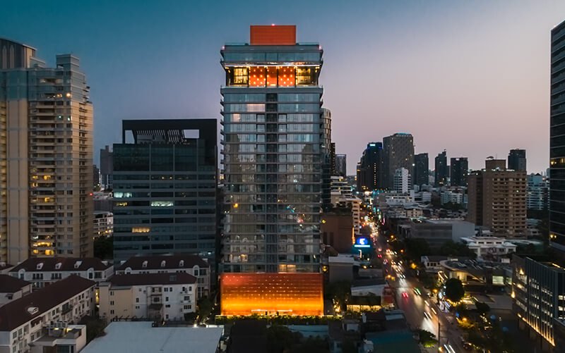 Slim high-rise with orange-lit crown above a busy lit street at dusk