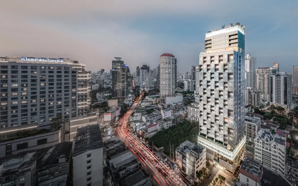 Dusk aerial of a white chequered-balcony tower beside red traffic trails on Thonglor
