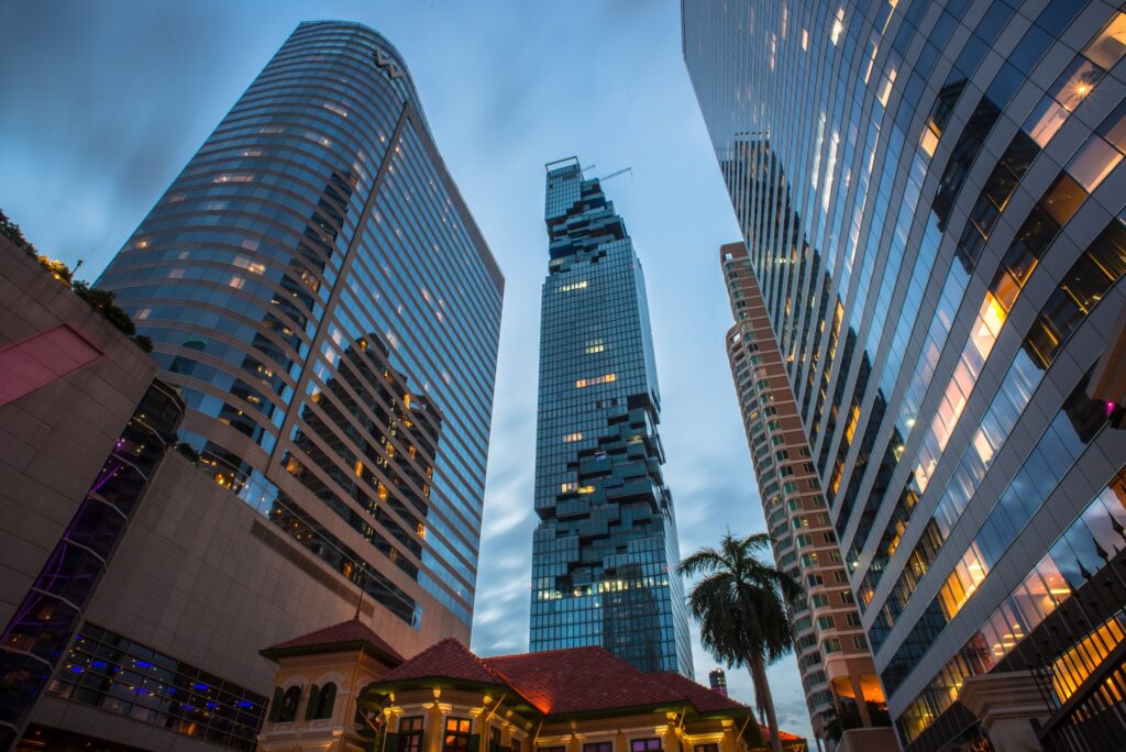 Looking up at glass office towers and the pixelated MahaNakhon spire past palm trees