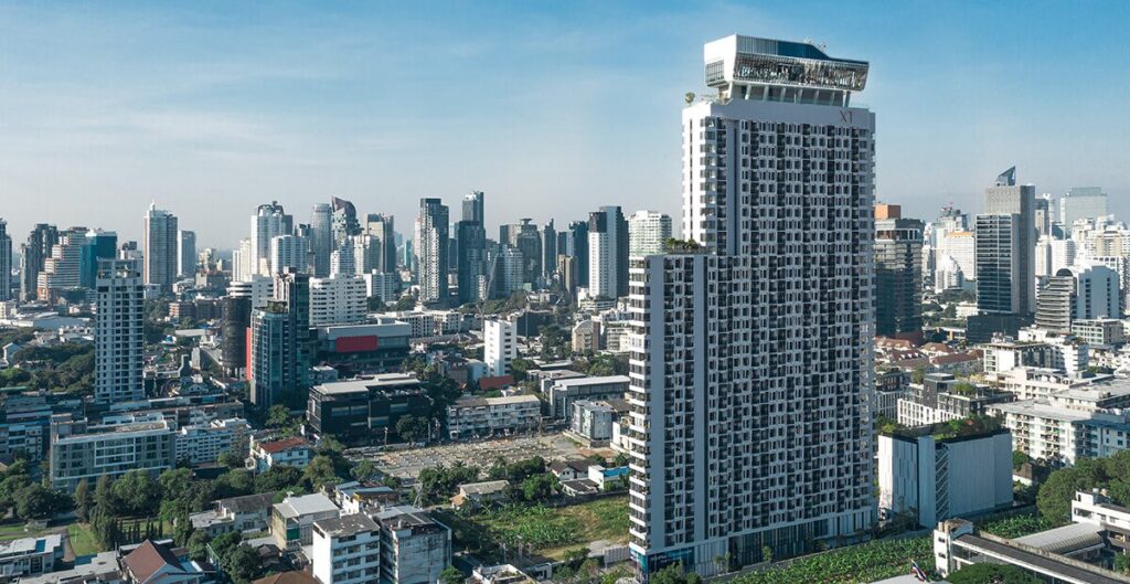 Tall grey residential tower rising above low-rise rooftops under a clear blue sky