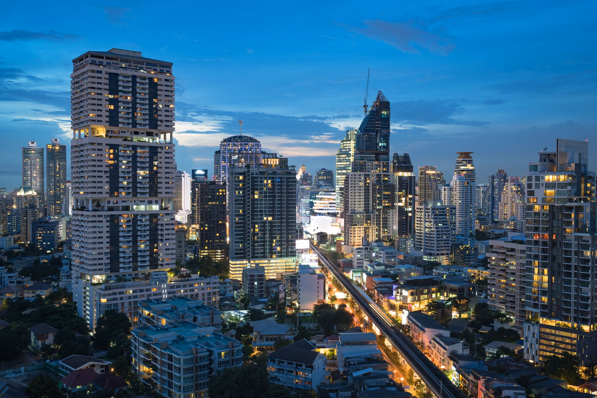 Dusk Bangkok skyline from above, lit condo towers and traffic-streaked road below