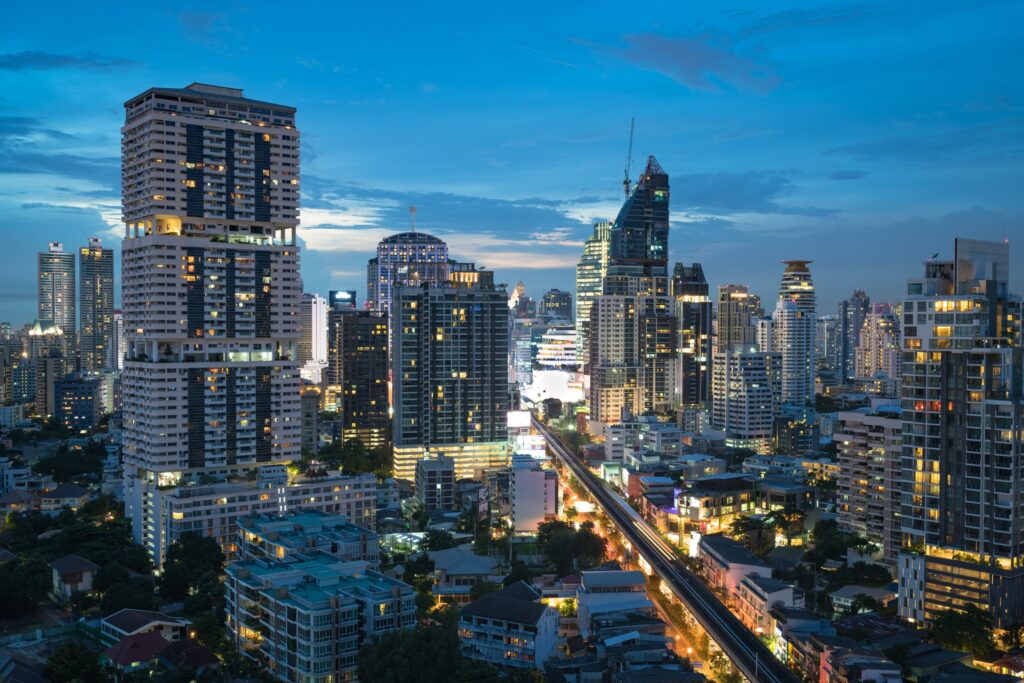 Wider dusk aerial of Phrom Phong towers, glowing windows and busy road at blue hour