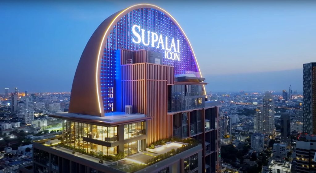 Render of arched illuminated Supalai Icon crown sign atop a lit tower at twilight