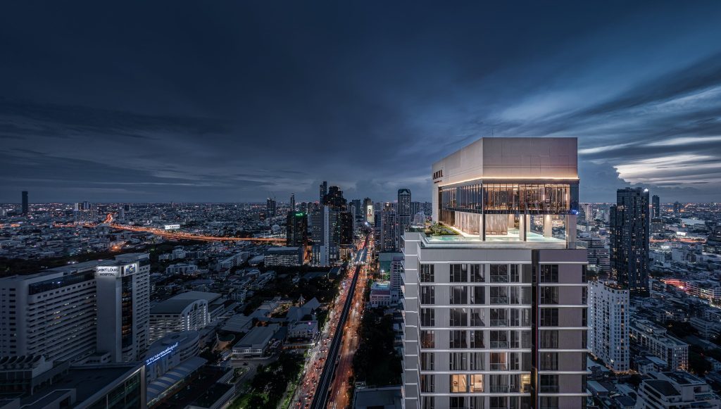 Night render of a slim tower's lit rooftop terrace above the dark Sathorn cityscape